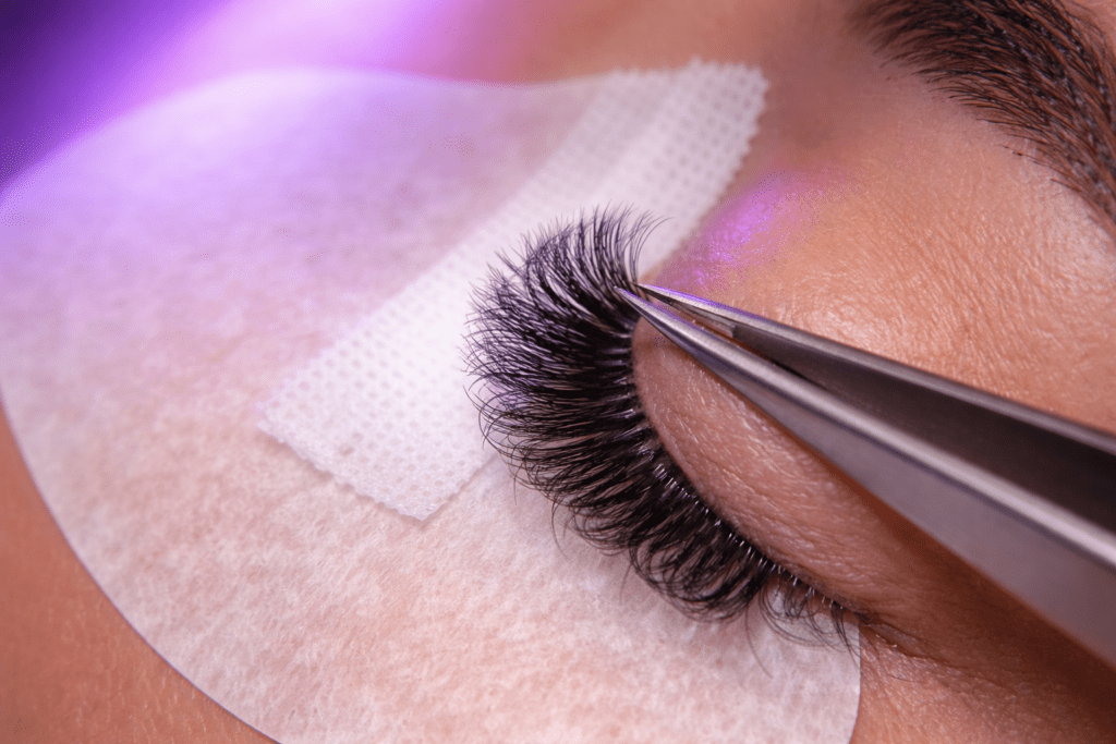 LED lash extensions being applied with tweezers under purple LED curing light at Lashes On Point Melbourne